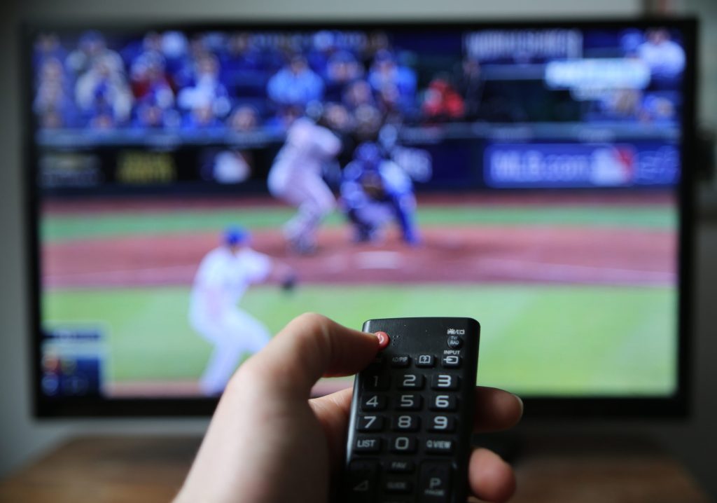 A hand holding the remote controller against the blurred TV screen/Baseball broadcast Hand holding the remote controller against the blurred TV screen/Baseball broadcast